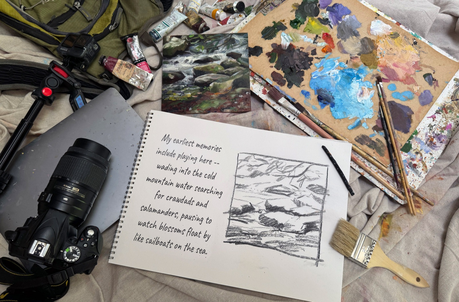 A painter's collage — backpack, paint tubes, a small painted study of a river, palette, camera, and an open sketchbook with a handwritten field note