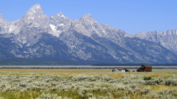 Reference photo — the tiny Mormon Row homesteads scattered across the vast sage flats beneath the towering, snow-dusted Teton range
