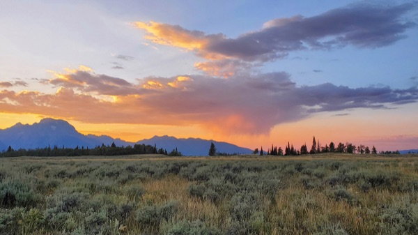 Reference photo — an orange sunset with a rain shower over the Teton range, Mount Moran to the left above the sage flats