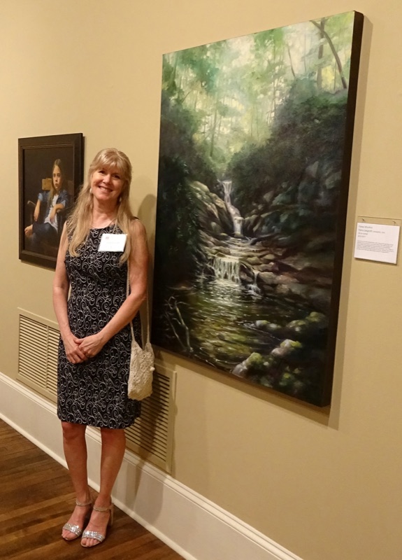 Trisha Selgrath standing beside her large oil painting of an Appalachian Mountain waterfall at a national juried museum exhibition
